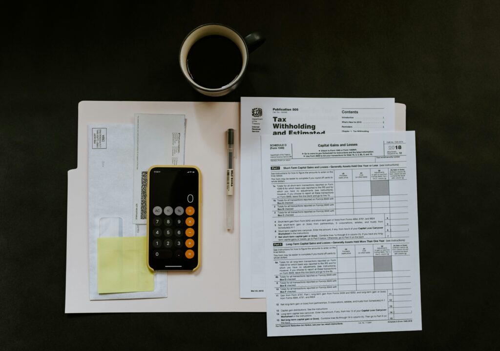 An overhead view of financial documents, a calculator on a phone, and a cup of coffee, representing the process of calculating business taxes like NZ GST.